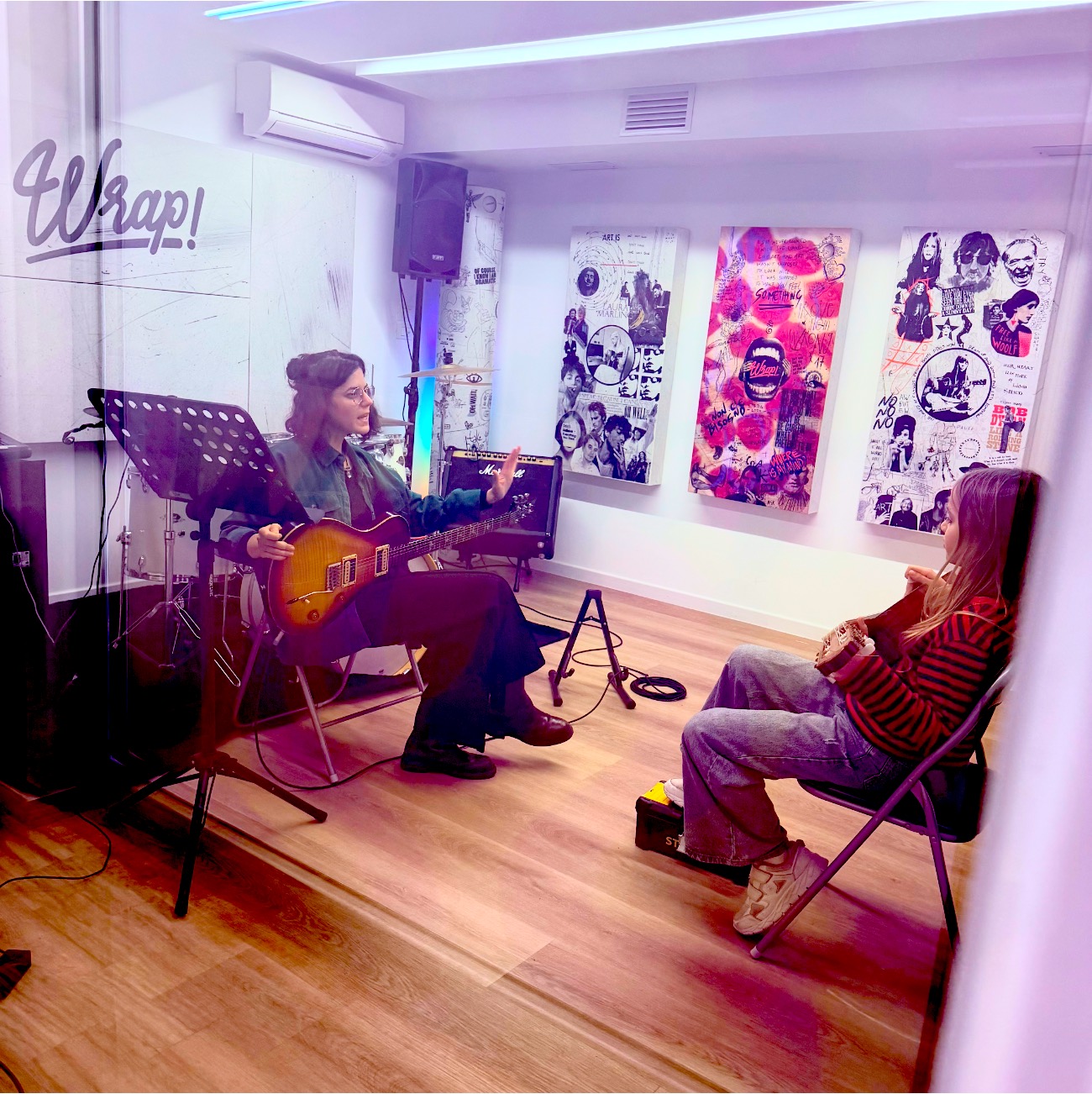 Una lezione di chitarra da Wrap: l'insegnante con la chitarra elettrica e l'allieva seduta di fronte